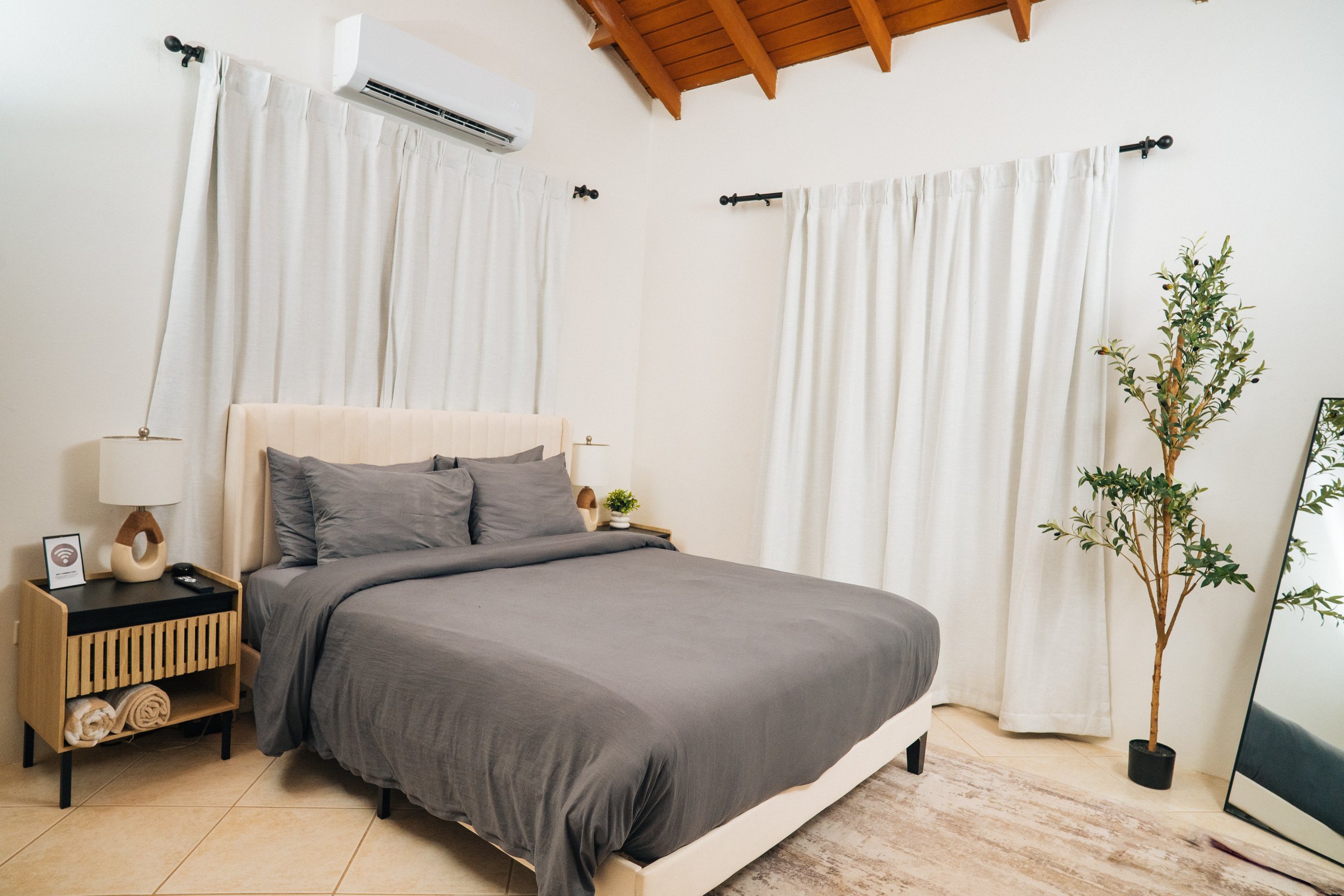 Bedroom with grey bedding, natural wood bedside tables, and a leafy plant